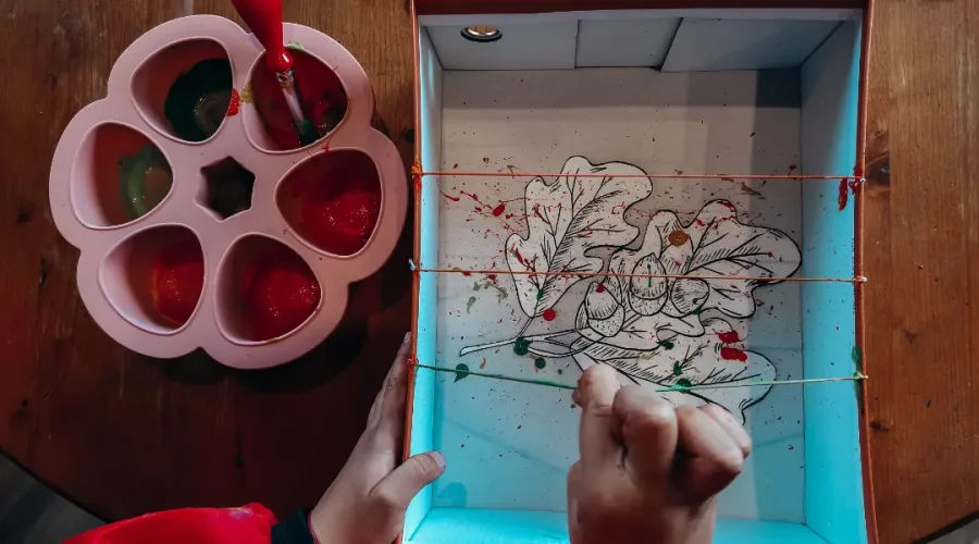 Bocaux en verre remplis de teintures végétales violettes, rouges et jaunes, posés sur une table en bois avec des fleurs et des feuilles.